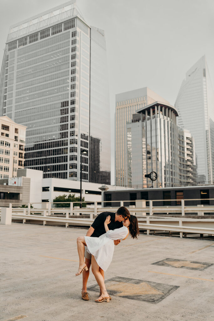 Photo of couple dipping on a parking garage rooftop in uptown charlotte with skyline in the background