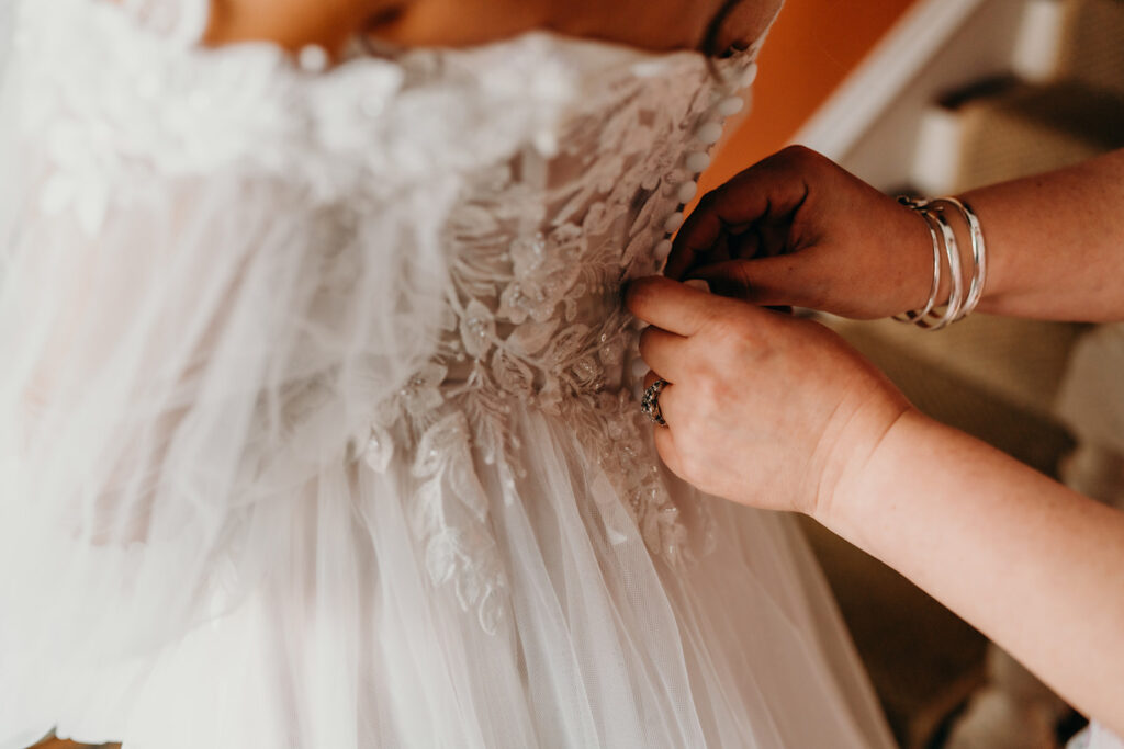 close up photo of hands buttoning wedding dress