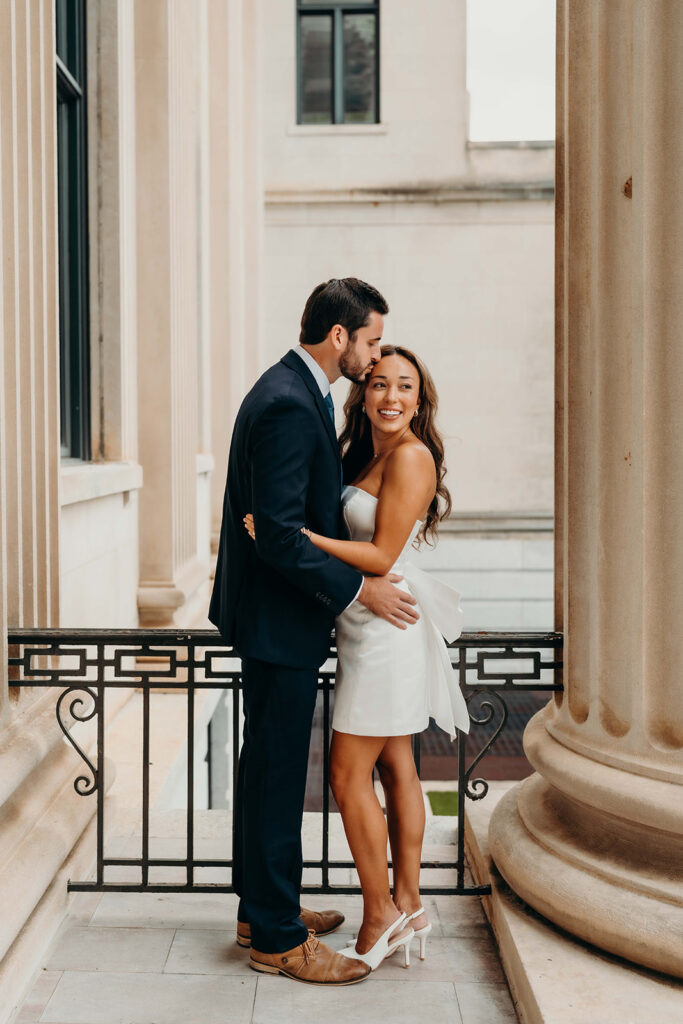 couple in white dress and navy blue suit and tie at classic courthouse building in uptown charlotte Timeless Engagement Photos in Uptown Charlotte