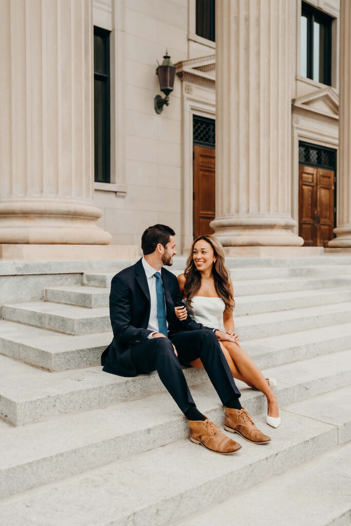 couple in white dress and navy blue suit and tie at classic courthouse building in uptown charlotte Timeless Engagement Photos in Uptown Charlotte