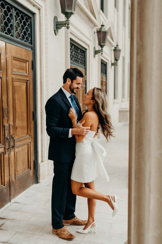 couple in white dress and navy blue suit and tie at classic courthouse building in uptown charlotte Timeless Engagement Photos in Uptown Charlotte