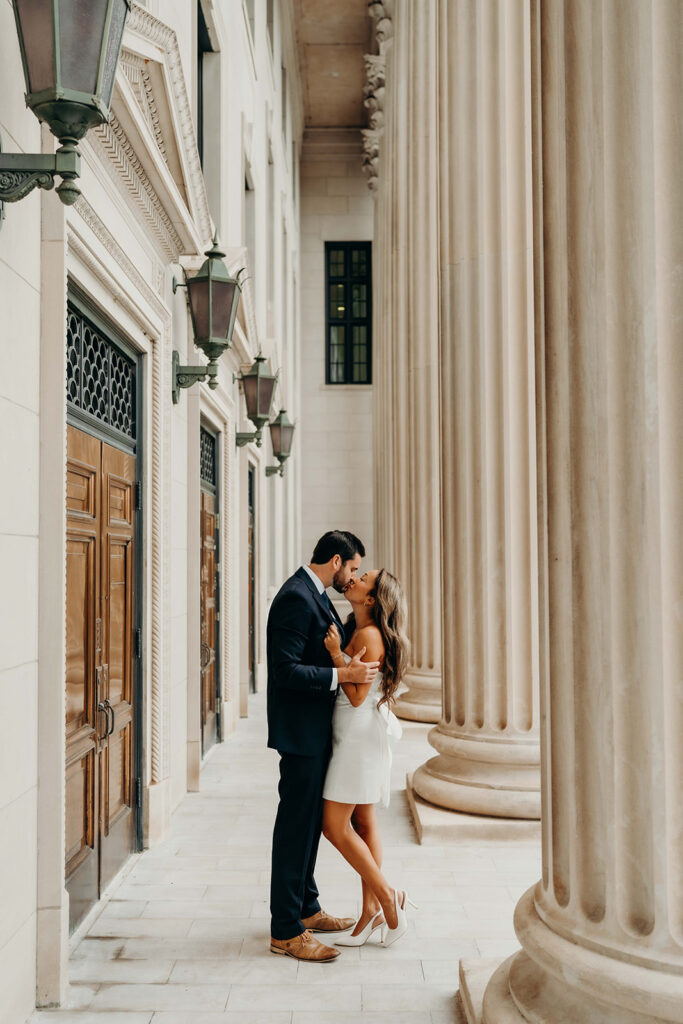 couple in white dress and navy blue suit and tie at classic courthouse building in uptown charlotte Timeless Engagement Photos in Uptown Charlotte