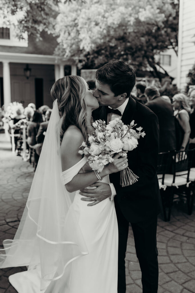 Summer wedding ceremony in secret private courtyard on a sunny day with lush greenery and blue flowers walking down aisle