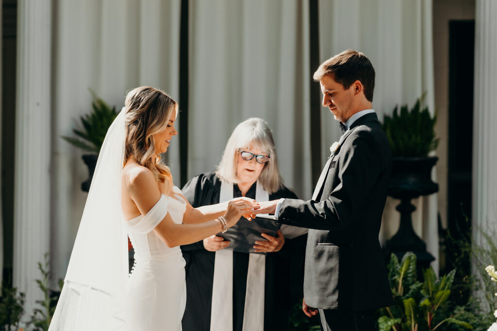 Summer wedding ceremony in secret private courtyard on a sunny day with lush greenery and blue flowers walking down aisle