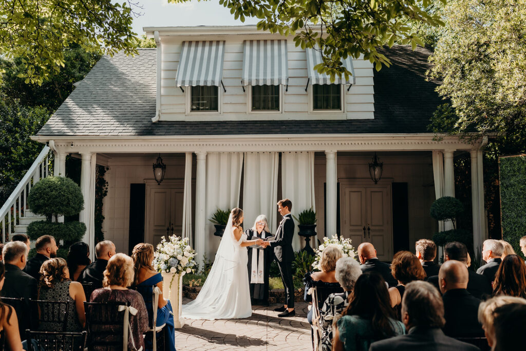 Summer wedding ceremony in secret private courtyard on a sunny day with lush greenery and blue flowers walking down aisle