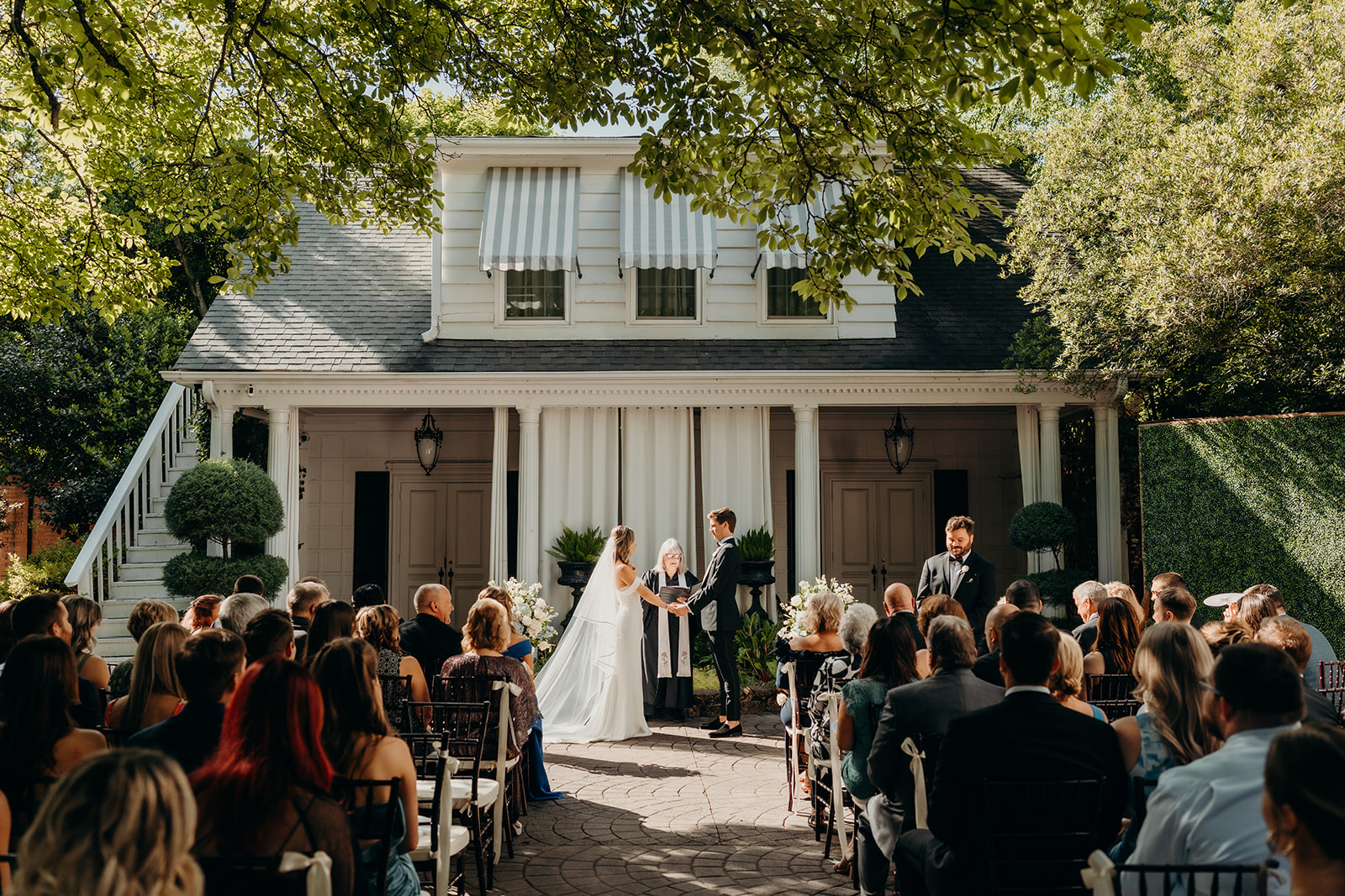 Summer wedding ceremony in secret private courtyard on a sunny day with lush greenery and blue flowers walking down aisle