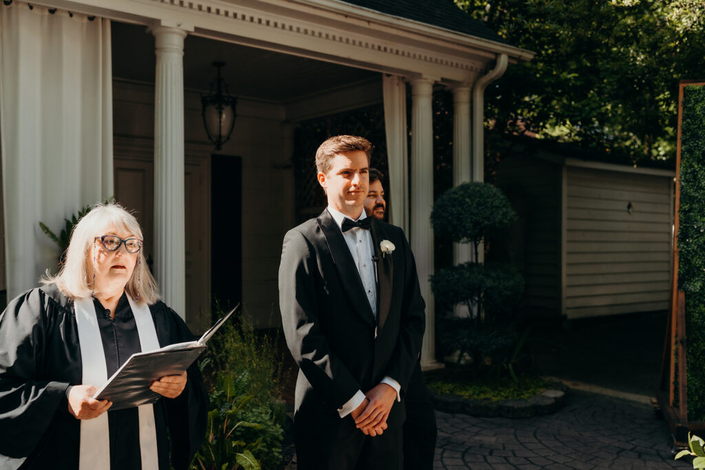 Summer wedding ceremony in secret private courtyard on a sunny day with lush greenery and blue flowers walking down aisle