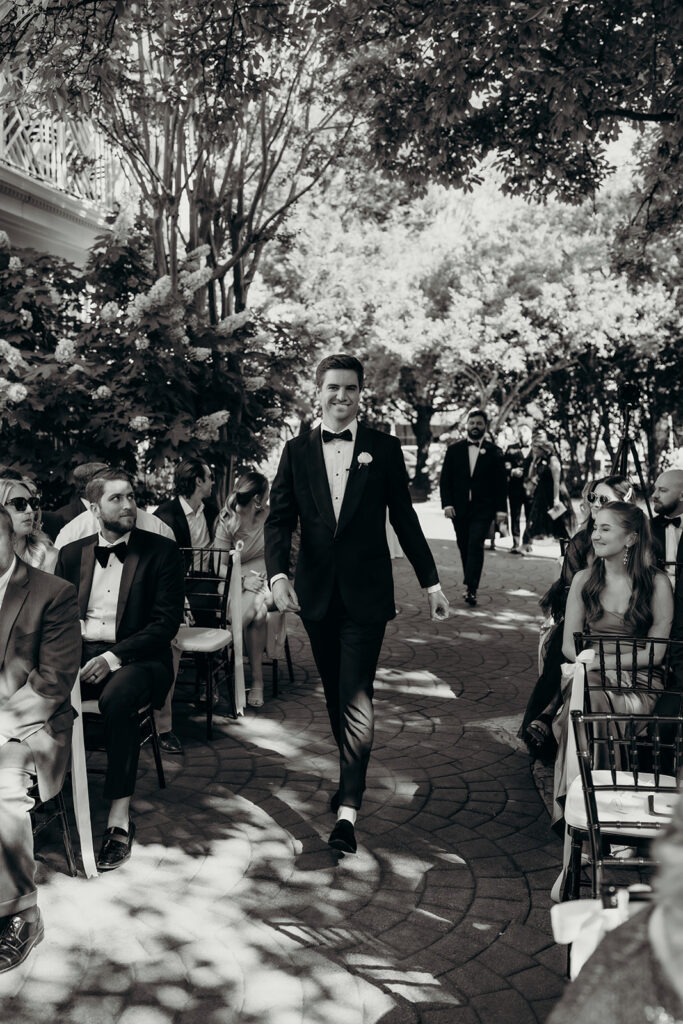 Summer wedding ceremony in secret private courtyard on a sunny day with lush greenery and blue flowers walking down aisle
