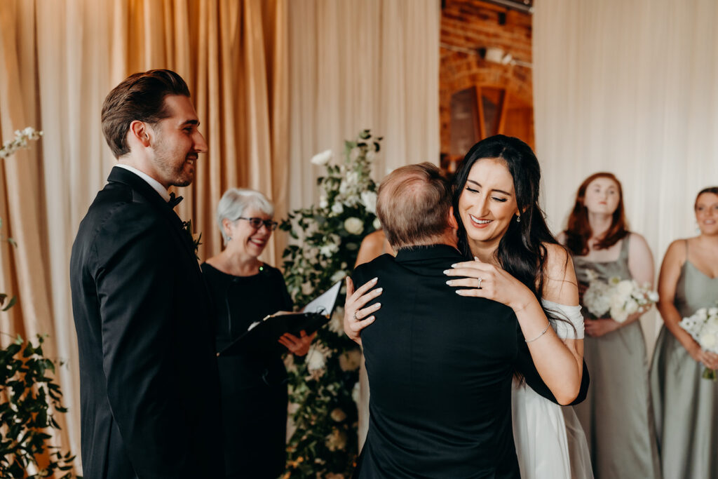 bride hugging dad as he gives her away during ceremony at melrose knitting mill