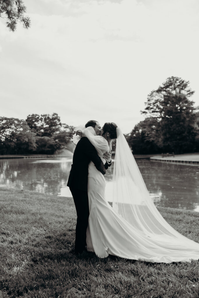 Bride and groom first kiss in front of the pond at their rose hill estate wedding