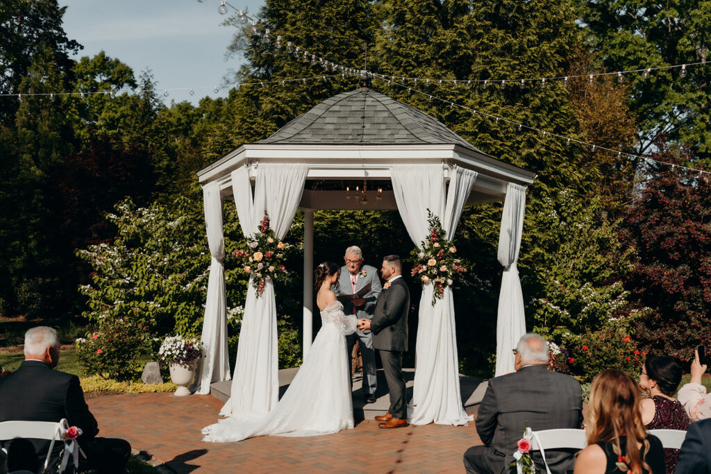 bride and groom during their ceremony sharing vows in front of the gazebo