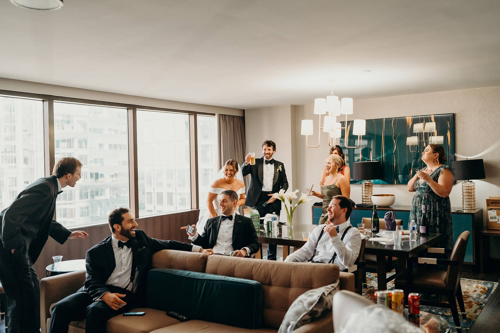 bride and groom having fun with wedding party in hotel room with a cheers