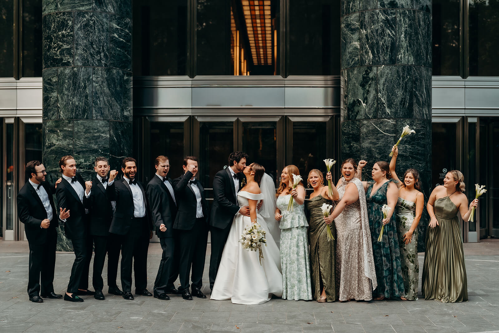 wedding party celebrating as bride and groom kiss
