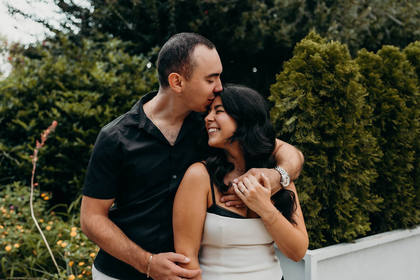 Couple snuggled up together with arms wrapped around each other while he kisses her forehead