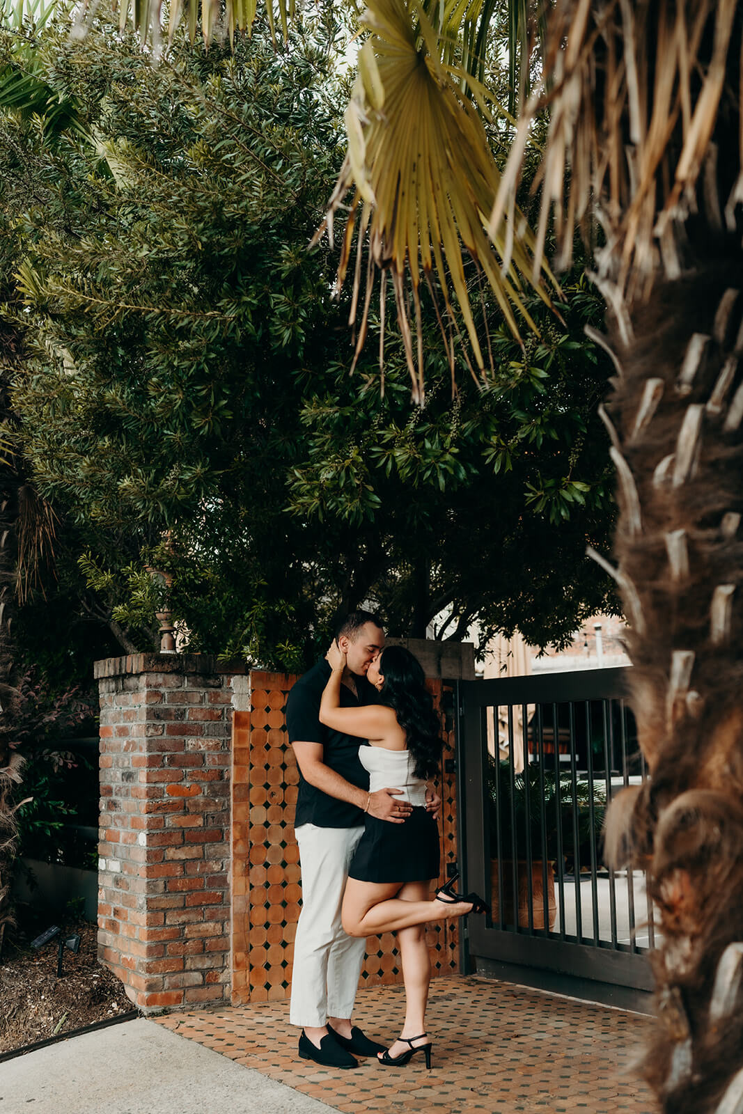Photo of couple standing at the front gate of Mulino during their Melrose Knitting Mill Engagement Session while they lean in for a kiss