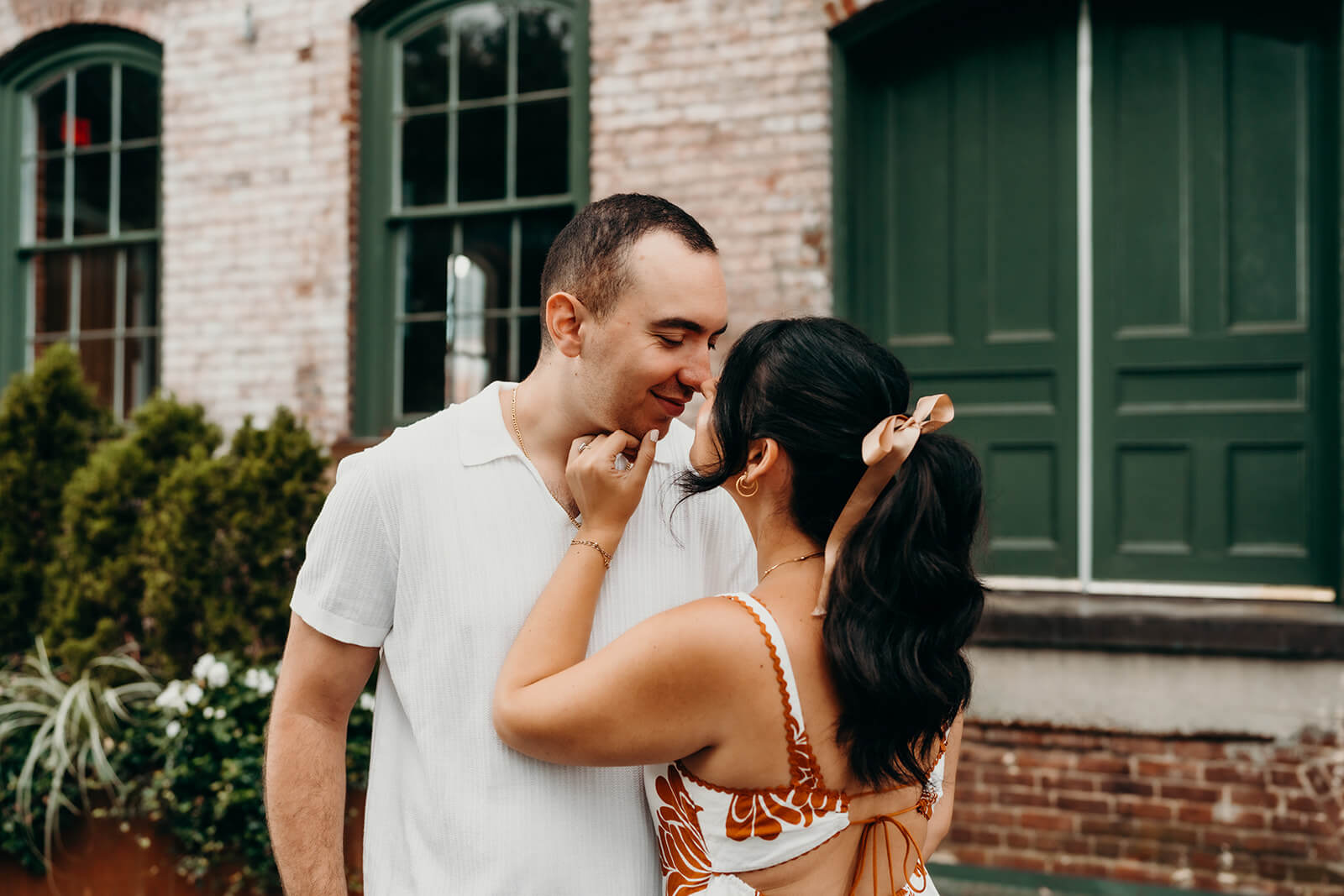 Photo of couple where she is grabbing his face and pulling him in for a kiss during a Melrose Knitting Mill Engagement Session