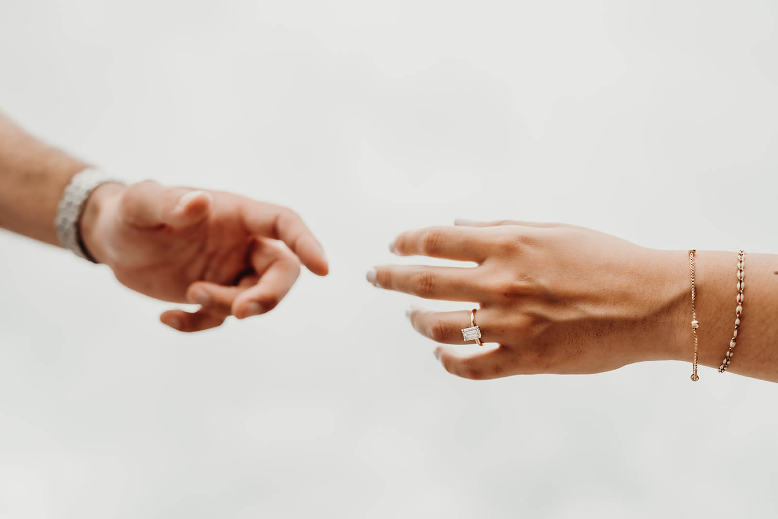 couple extending their hands towards each other while showing her engagement ring