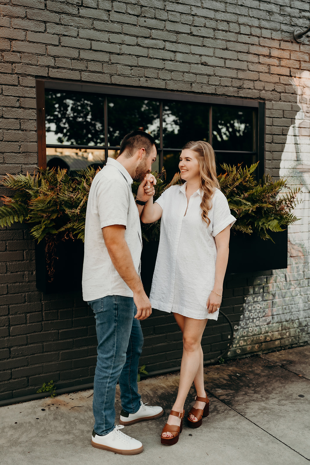 couple he is kissing her hand on the sidewalk