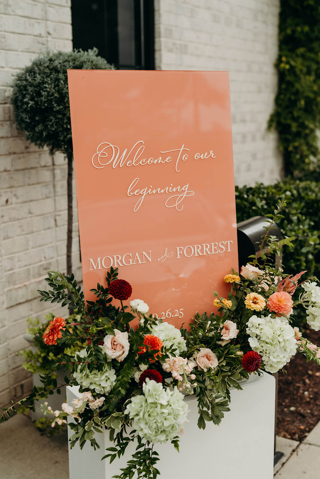 detail photo of the couples welcome sign thats pink with flowers under it