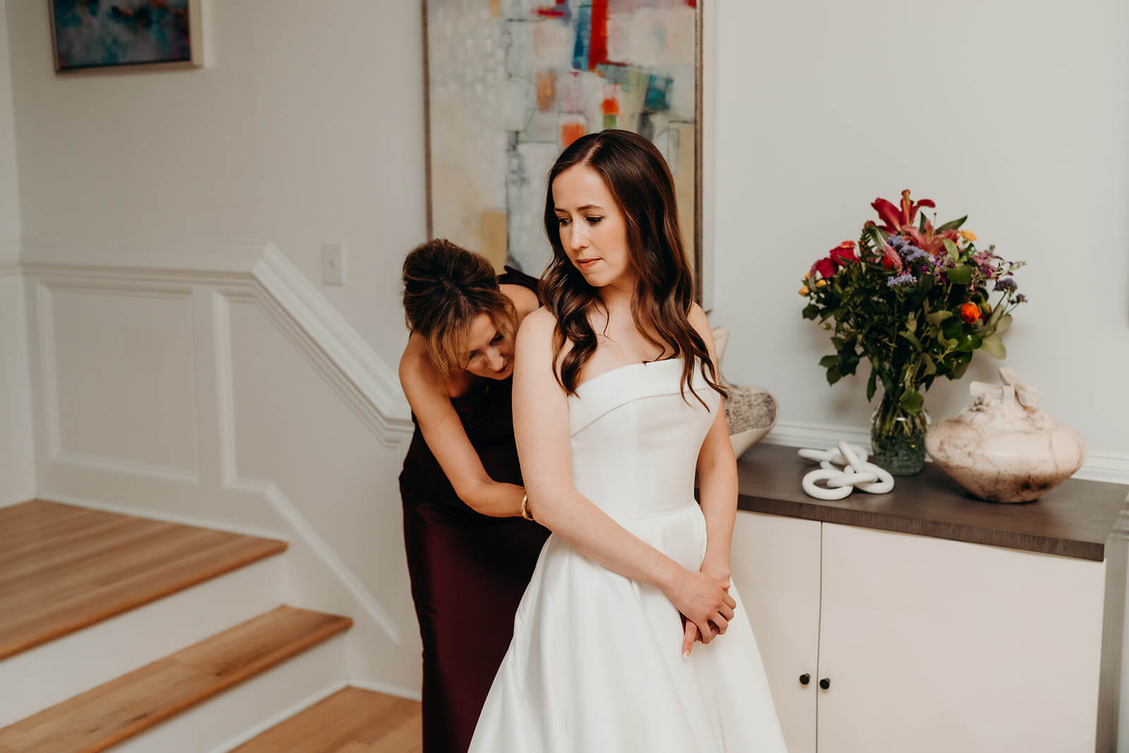 bride getting ready while mom helps her into her dress